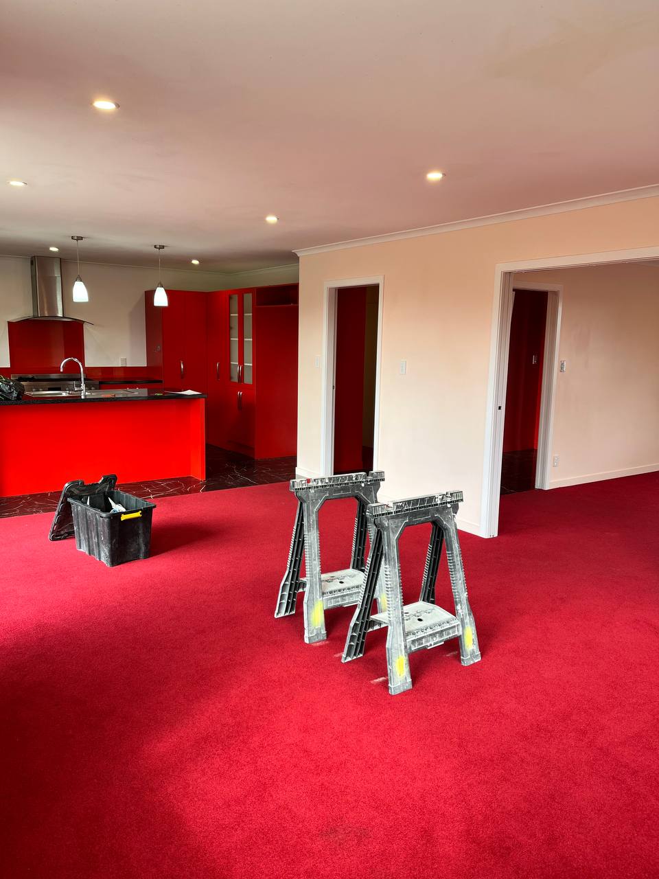 Living room before painting - red carpet, beige walls, painting trestles set up